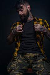 Bearded man with tattoos on his hands and neck wearing yellow black shirt and army pants