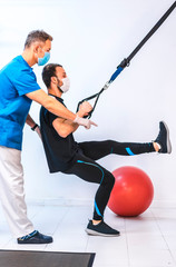 Physiotherapist with mask and a patient doing stretches with rubber bands. Physiotherapy with protective measures for the Coronavirus pandemic, COVID-19. Osteopathy, sports chiromassage