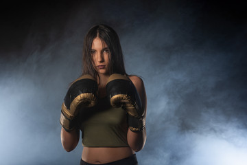 Fototapeta premium Closeup portrait of a female boxer posing with boxing gloves and looking at the camera with a smokey background