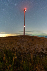 starry sky with an electric windmill in the middle of a natural landscape at the sunrise