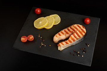 Grilled salmon steak with a lemon, tomatoes and salad on a slate plate.