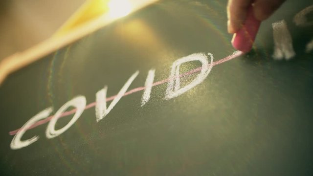 Crossing out COVID-19 text written with chalk on a blackboard, vaccine related conceptual slow motion shot