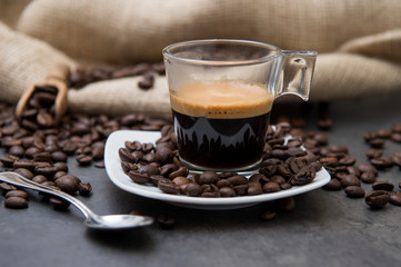 Italian espresso coffee in a glass cup on a black floor with coffee beans cutting light and frontal view