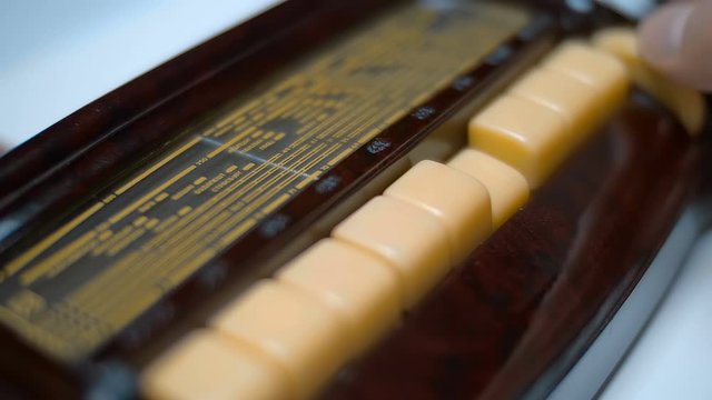 A man is looking for a music station on an old beautiful antique radio, the arrow moves along the scale, the buttons switch different frequency ranges and push button to auto-adjust the frequency of t