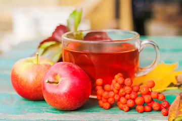 the concept of an autumn day. on the table is a glass Cup of tea, a bunch of Rowan, apples, fallen leaves in the open air