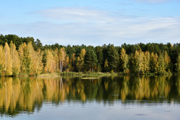 Fototapeta na wymiar Autumn forest on the lake is full of bright colors against a blue clear sky, reflection in calm water