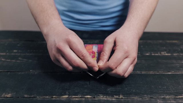 Man opening package with halva on black wooden kitchen table. Unhealthy fat tasty sweets, food, diet, nutrition, overweight concept.