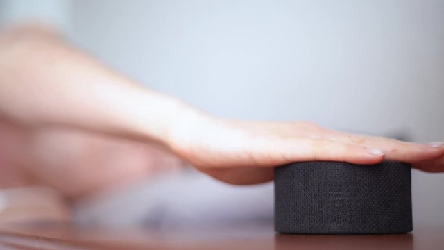 Young woman wakes up with alarm clock working on smart portable device. Turning off the alarm clock with the touch of a woman's hand