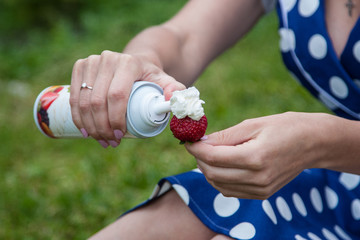 
The girl applies cream on a ripe strawberry.