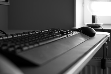 A black and white photo of a keyboard and mouse on a desk with no people in a home office. Showing the feeling of loneliness when working from home during quarantine