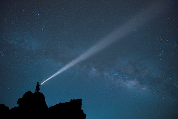 Night landscape of a man with a powerful military flashlight illuminating the starry sky leaving a...
