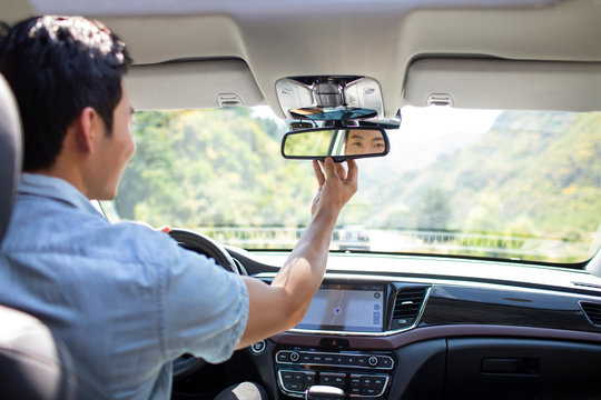 Young man adjusting rear-view mirror in car - Powered by Adobe
