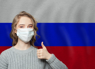 Happy woman in face mask holding thumb up on Russian flag background. Flu epidemic and virus protection concept