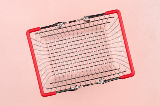 Empty metal shopping basket with red handles, on pink background. Top down view, selective focus on the bottom.
