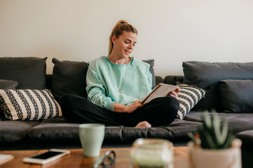 Obraz premium Happy beautiful woman watching videos or enjoying entertainment content on a tablet sitting on the sofa. home working