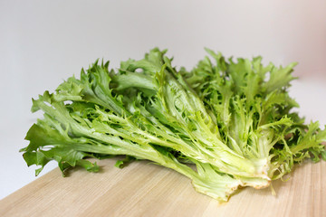 A bunch of fresh lettuce on the cutting wooden board on the white background. Seasoning greens on the table. Healthy vegetarian food. An ingredient for salad.