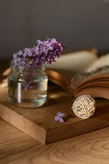 Fototapeta na wymiar a sprig of lilac in a glass jar of water stands on a wooden table against the background of an open book