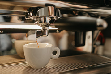 Espresso brewing in a professional espresso machine in a coffee shop. A close-up of a coffee pouring in a white cup from a coffee machine in a cafe.