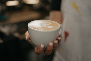 A female barista holds a cup of hot latte in her hand in a cafe. A waitress preparing a customer order.