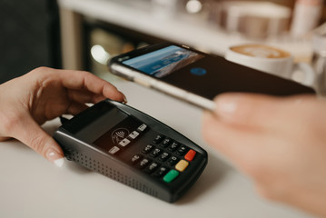 A lady paying for her latte with a smartphone by contactless NFC technology in a cafe. A female barista holds out a terminal for paying to a client in a coffee shop.
