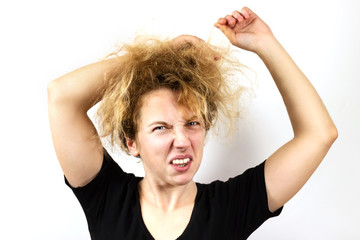 Close-up of a sad girl with disheveled yellow dyed hair pulling her hair and grimacing. On white background. An emotion of frustration and discontent. Bad hair day.