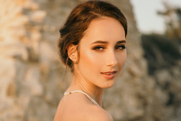 Portrait of beautiful young smiling girl in the white dress in greek style walking along the sea promenade. Summer, sunset time. Bride wedding at sea 