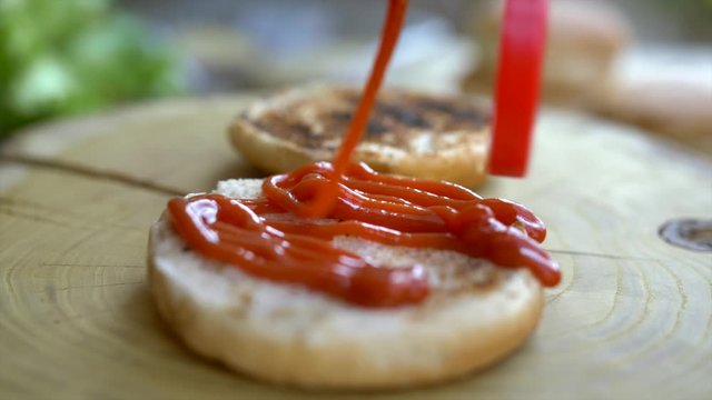 Close up of professional chef cooks a delicious burgers at fast food restaurant. Female chef in gloves puts ketchup on three rosted breads for burgers