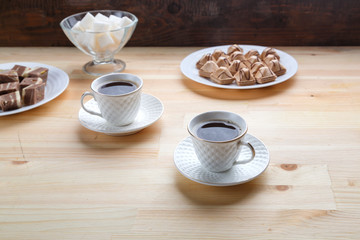Two cups of coffee on a wooden table with croissants and sugar.