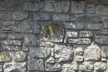 Wall of gray stones of different sizes, irregular glued with cement but protruding from the wall.