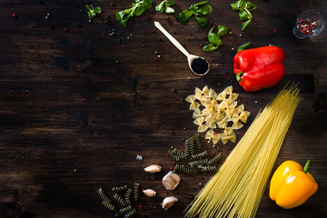 Various sorts of pasta on top of a dark wooden background. Farfalle, fusilli, spaghetti, bell...