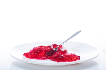 Red jelly in a white plate with a spoon. Eat jelly from a plate. Isolate