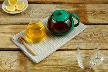 Kettle with brewed tea and honey with lemon on the table.