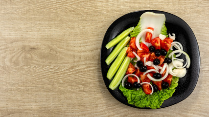 Healthy salad with tomatoes, cucumber, black olives, onion, salad. Concept for healthy nutrition. Light wooden background. Copy space