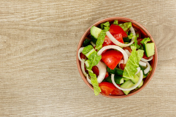 Still life of tomatoes, cucumbers, onions, lettuce in a brown cup on a light wooden background with copy space. Healthy eating. Top view
