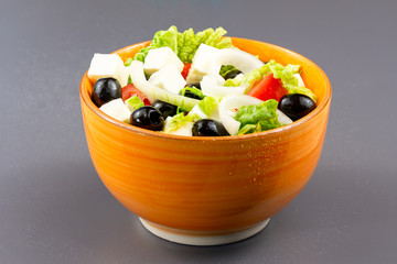 Healthy salad with tomatoes, cheese, olives, onions, lettuce in a ceramic cup on a grуy wooden background. Healthy eating concept
