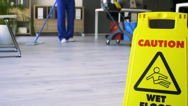 Caution sign with text CAUTION, WET FLOOR and janitor mopping the office