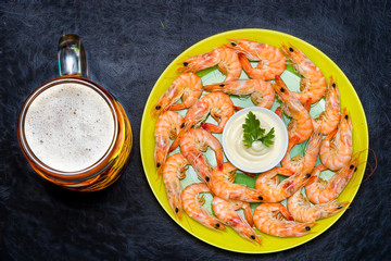 A mug of cold beer with boiled shrimp on a plate on a black background.