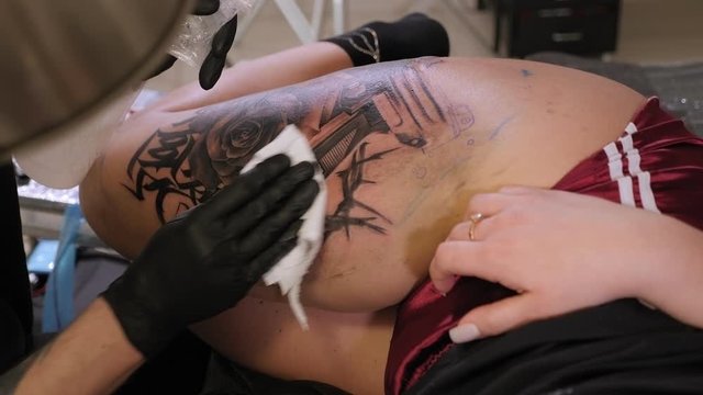 The tattoo master atomises a sterile solution on a ready-made new tattoo on the girl's leg. The process of tattooing ink in a professional tattoo parlor.