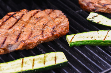 Steak and zucchini being grilled on barbecue