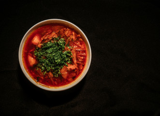 Red borsch on a black background. Borsch with vegetables and tomato. Ukrainian traditional cuisine.
