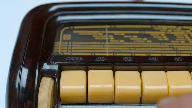 A man is looking for a music station on an old beautiful antique radio, the arrow moves along the scale, the buttons switch different frequency ranges and push button to auto-adjust the frequency of t