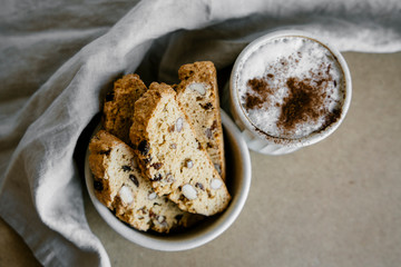 Freshly baked almond biscottis with cup of cappuccino on wooden background. Breakfast food concept. 