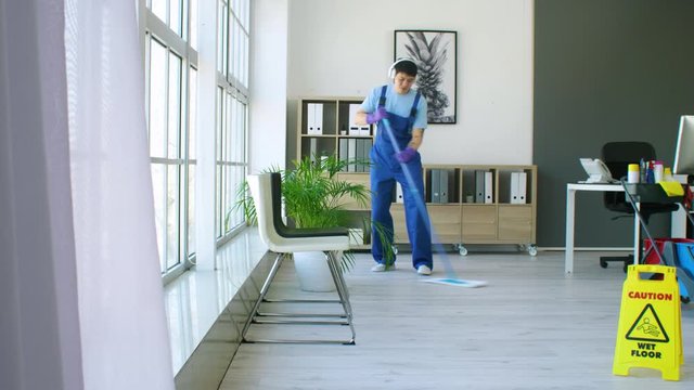 Male Asian janitor listening to music while mopping floor in office