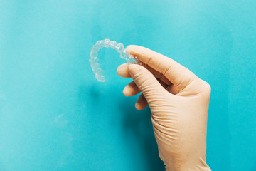 Doctor's hand teaches clear dental aligners on sky-blue background with copy space