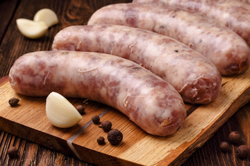 Raw homemade sausages with garlic cloves and spices on wooden table.