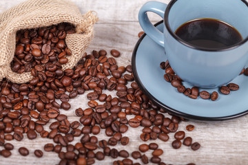 Cup of coffee and bag with coffee grains on a wooden surface