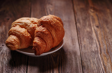 Freshly croissants on white plate on dark wooden table, empty place for text. Sweet and tasty dessert. Baking concept.