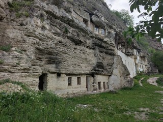 Fototapeta na wymiar Old rock monastery in the mountains. Two floors. Green grass. Layered rock