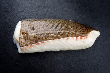 Rohes norwegisches Skrei Kabelja Fisch Filet mit Haut als closeup auf einem schwarzen Board mit...