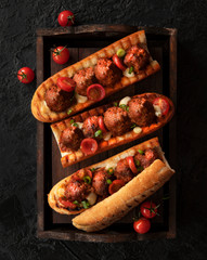 Sandwich with meatballs on a baguette, with melted cheese, tomato sauce, parsley and Parmesan cheese on top. Traditional Italian meatballs baked in a baguette on a wooden tray on a black background. T - 351351989